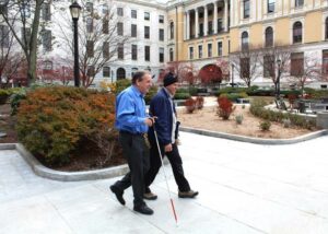 ADA Coordinator Carl Richardson and Joe Kolb, who works at the Carroll Center for the Blind, walk near the State House. (Photo/Courtesy of Greg Turner of the Ball Consulting Group, LLC.)