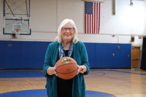 Jan Bryan stands on the Oak Middle School gymnasium floor, where she started playing basketball 66 years ago. (Photo/Evan Walsh)